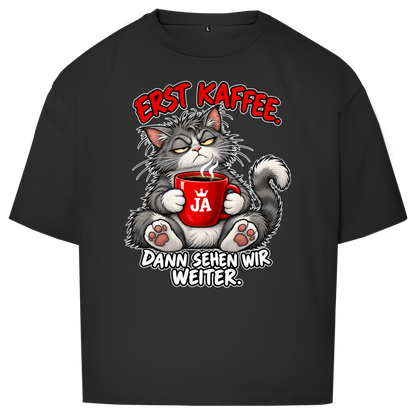 JA Erst Kaffee – Oversize-Shirt in Schwarz, Vorderansicht, Frontdruck: Grimmige Katze mit roter Tasse: „Erst Kaffee. Dann sehen wir weiter.“