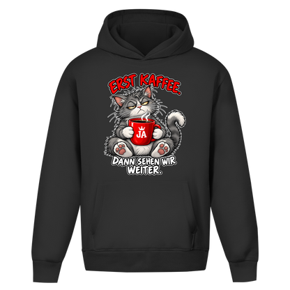 JA Erst Kaffee – Oversize-Hoodie in Schwarz, Vorderansicht, Frontdruck: Grimmige Katze mit roter Tasse: „Erst Kaffee. Dann sehen wir weiter.“
