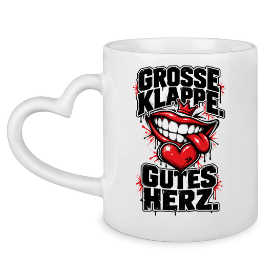 JA Große Klappe, gutes Herz – Tasse mit Herzhenkel in Weiß, Vorderansicht, Aufdruck: Markenspruch „Große Klappe. Gutes Herz.“ mit rotem Mund und Herz