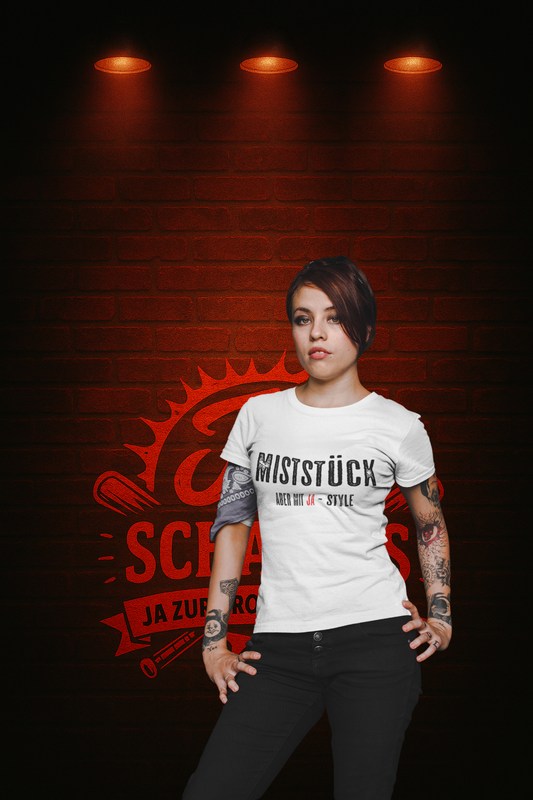 Frau mit Tattoos trägt weißes Statement-T-Shirt „Miststück – Meet me with Style“ vor rotem Backstein-Hintergrund im rebellischen JA-Style von JA-SCHAEFERS.DE